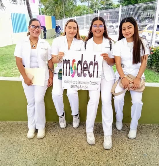 Prestadoras de servicio social sosteniendo letrero de MODECH